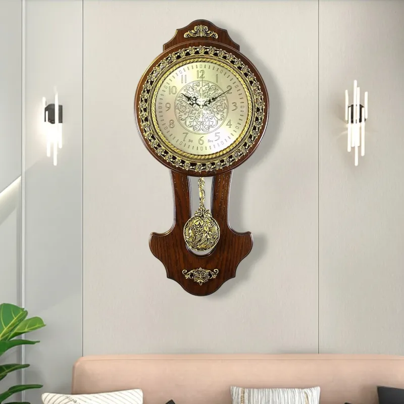 ساعة حائط كلاسيكية مزينة بزخارف ذهبية أنيقة مع بندول زخرفي. لها إطار مصنوع من الخشب البني الداكن، وهو مزين بزخارف ذهبية معقدة تعطي الساعة مظهراً فاخراً يناسب الديكورات الكلاسيكية.