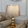 أباجورة طاولة ذهبية بتصميم كرات وقماش بني فاخر، إضاءة جانبية أنيقة.