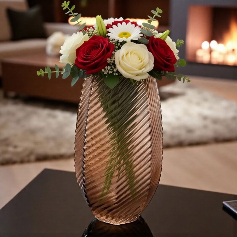 فازة زجاجية عسلية اللون بتصميم حلزوني مضلع، مناسبة للديكور المنزلي الأنيق والعصري، مزخرفة بباقة من الورد الأحمر والأبيض