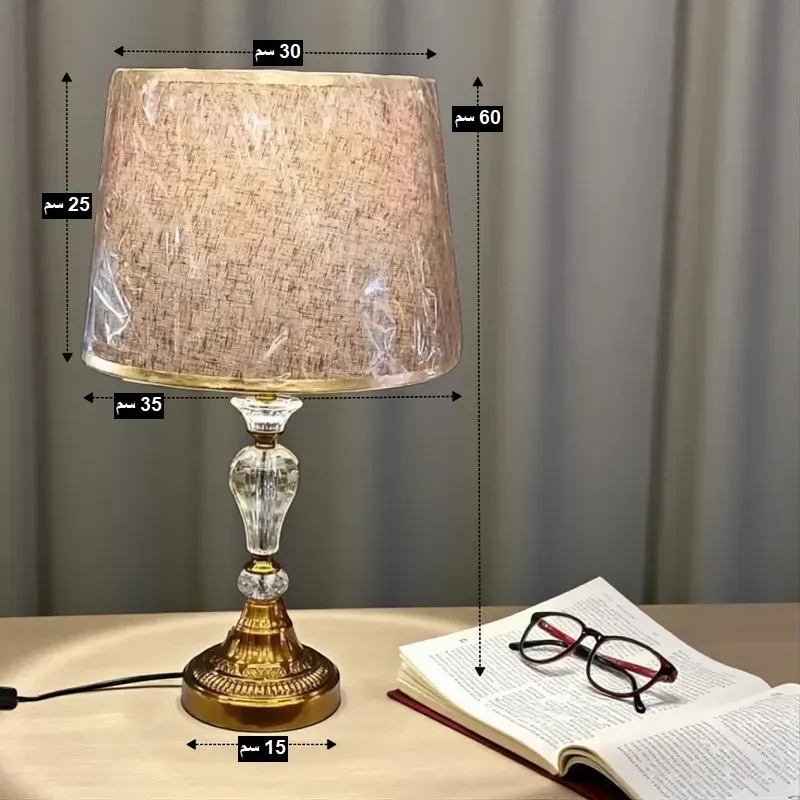 أبعاد أباجورة الكريستال: الارتفاع الكلي 60 سم، عرض الشابو 35 سم من أسفل و 30 سم من أعلى، ارتفاع الشابو 25 سم، قاعدة معدنية دائرية بقطر 15 سم.