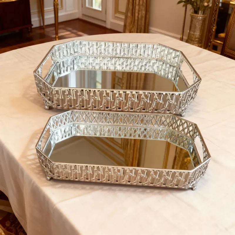 إخوان سرور الإضاءة الحديثة والديكور طقم صواني تقديم مزدوج، لون فضي، بتصميم هيكلي وزخرفة متشابكة، على سطح طاولة بمفرش بيج.