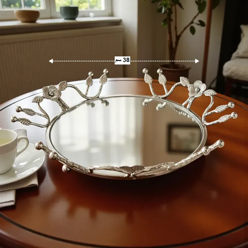 إخوان سرور الإضاءة الحديثة والديكور صينية تقديم فضية بيضاوية عاكسة كبيرة الحجم (38 سم) مزينة بزهور، تستخدم كقطعة ديكور على طاولة خشبية مستديرة.