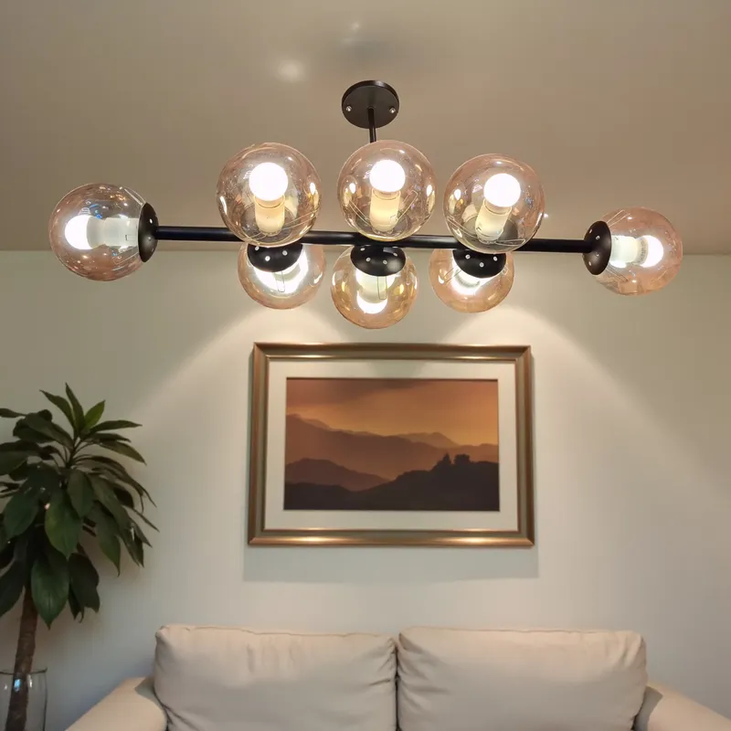 نجفة سقف عصرية بـ 8 كلوبات زجاجية عسلية دافئة معلقة فوق كنبة في غرفة معيشة بألوان هادئة.