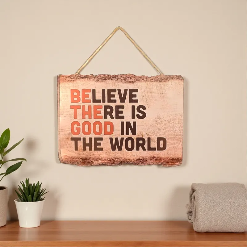 لوحة جدارية خشبية معلقة مكتوب عليها BELIEVE THERE IS GOOD IN THE WORLD، تصميم ريفي وألوان برتقالية وبنية، ديكور حائط إيجابي.