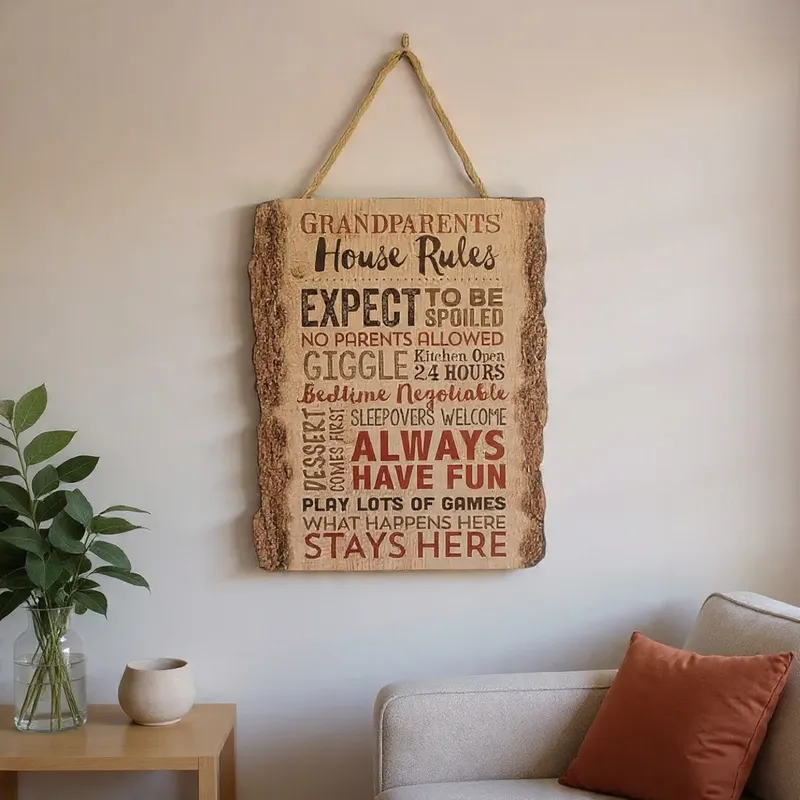 لوحة جدارية خشبية معلقة بعبارة "Grandparents House Rules"، بألوان بنية وحمراء، معروضة بجانب أريكة.