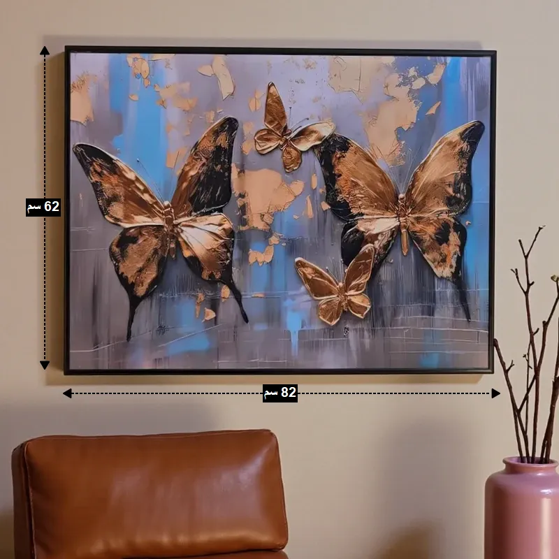 أبعاد اللوحة الفنية "فراشات ذهبية" 82 سم عرض و 62 سم ارتفاع، معروضة فوق كرسي جلدي.