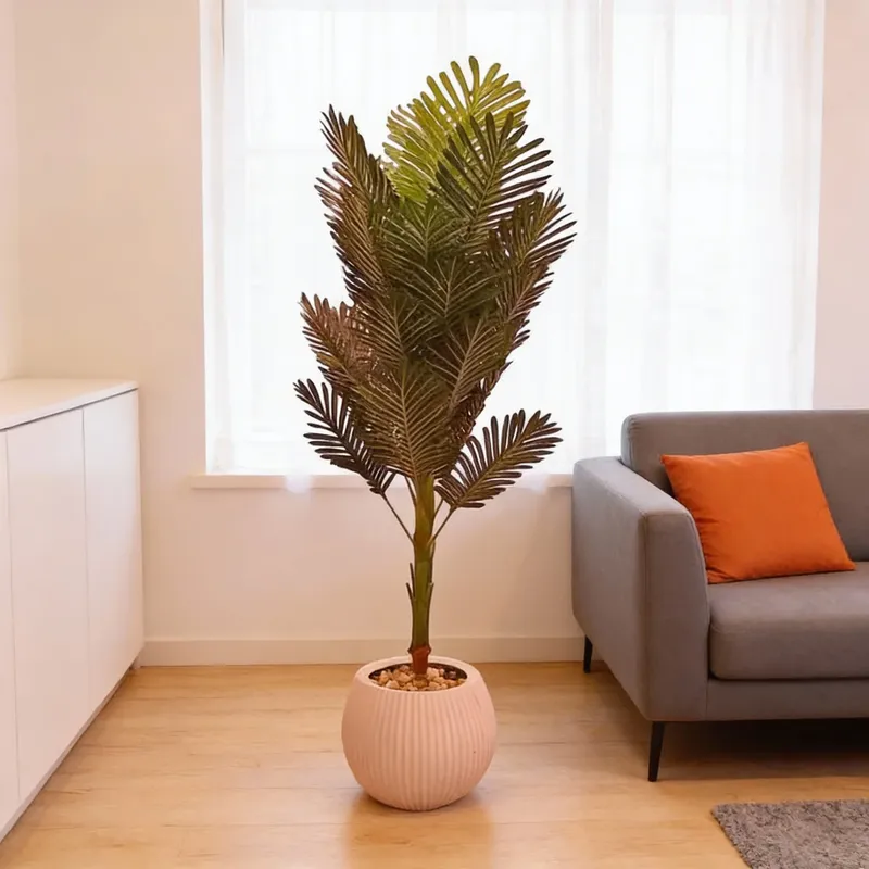 إخوان سرور الإضاءة الحديثة والديكور شجرة نخيل صناعية خضراء في إناء وردي، بجانب أريكة رمادية وخزانة بيضاء في غرفة معيشة عصرية.