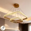 نجفة LED مودرن بتصميم مربع مزدوج باللون الذهبي اللامع، معلقة بأسلاك رفيعة في سقف غرفة معيشة عصرية، وتتضمن رمز التحكم عن بُعد.