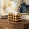 علبة مناديل سيراميك ذهبية فاخرة بتصميم كرات متراصة موضوعة بجانب لوحة فنية وكتب لديكور غرفة المعيشة.