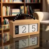 تقويم مكتبي خشبي أنيق بمكعبات أرقام ومقبض خرز أسود موضوع على طاولة زجاجية في مكتبة.