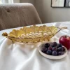 وعاء تقديم معدني ذهبي مفرغ فارغ بأرجل دائرية موضوع بجانب طبق صغير من العنب وتفاحة حمراء.