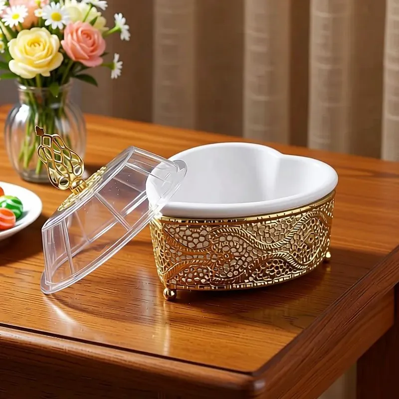 بونبونيرة سيراميك ذهبية على شكل قلب وغطاء أكريليك، موديل 029767 بونبونيرة ذهبية مفتوحة تظهر الإناء السيراميكي الأبيض الداخلي على شكل قلب مع غطاء أكريليك جانبي.