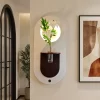 ديكور جداري بيضاوي بقاعدة فاتحة ورف بني داكن يحتوي على وعاء زجاجي مدمج وغصن ورد مضاء بالليد.
