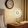 أباجورة ترابيزة ليد مودرن مضاءة بتصميم متداخل ذهبي بجوار سرير وساعة حائط لأجواء مريحة.