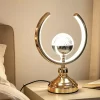أباجورة ترابيزة ليد مودرن بتصميم قوس ذهبي وكرة كريستال مضاءة على ترابيزة غرفة النوم.
