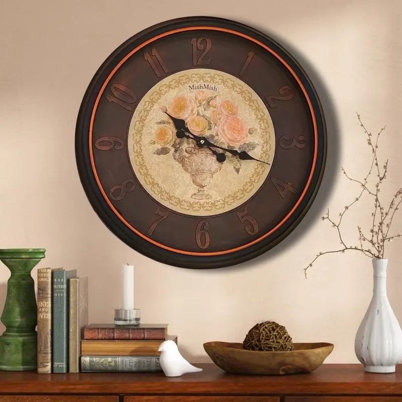 ساعة حائط دائرية ذات تصميم كلاسيكي باللون البني الداكن وإطار برونزي، تتميز بخلفية مزخرفة بنقشة زهور باللونين الوردي والأصفر داخل إناء أنيق. الأرقام العربية بارزة باللون البني، والعقارب سوداء تشير إلى حوالي الساعة الخامسة والربع. ساعة ديكورية أنيقة للمنزل أو المكتب.