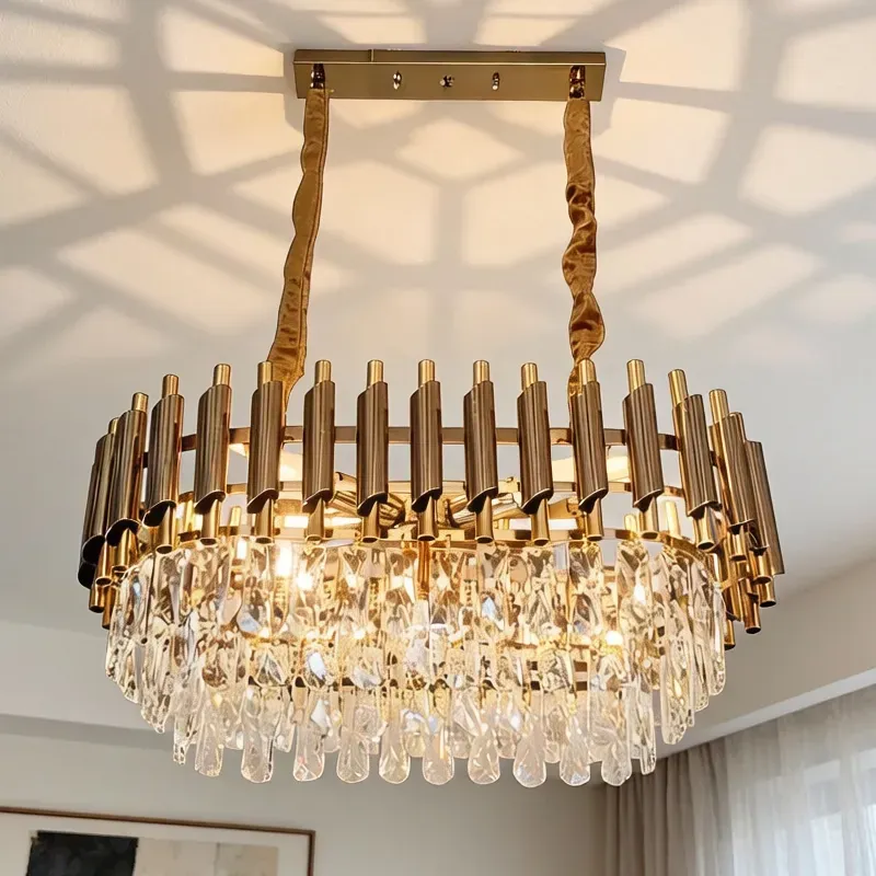 نجفة كريستال بيضاوية الشكل بهيكل ذهبي معلقة في سقف الغرفة تضفي إضاءة جذابة.